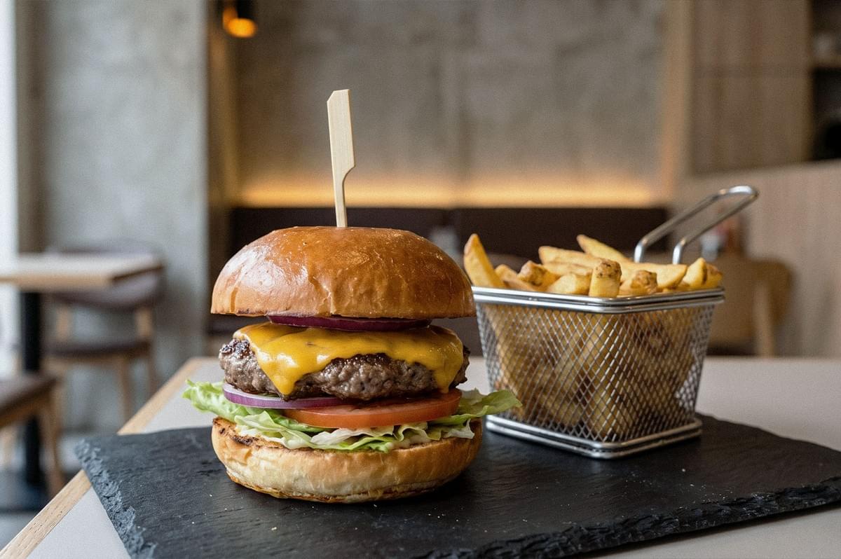 Cheeseburger with melted cheddar, lettuce, tomato, and red onion on a toasted bun, served with golden fries in a wire basket. Cheeseburger with melted cheddar, lettuce, tomato, and red onion on a toasted bun, served with golden fries in a wire basket.