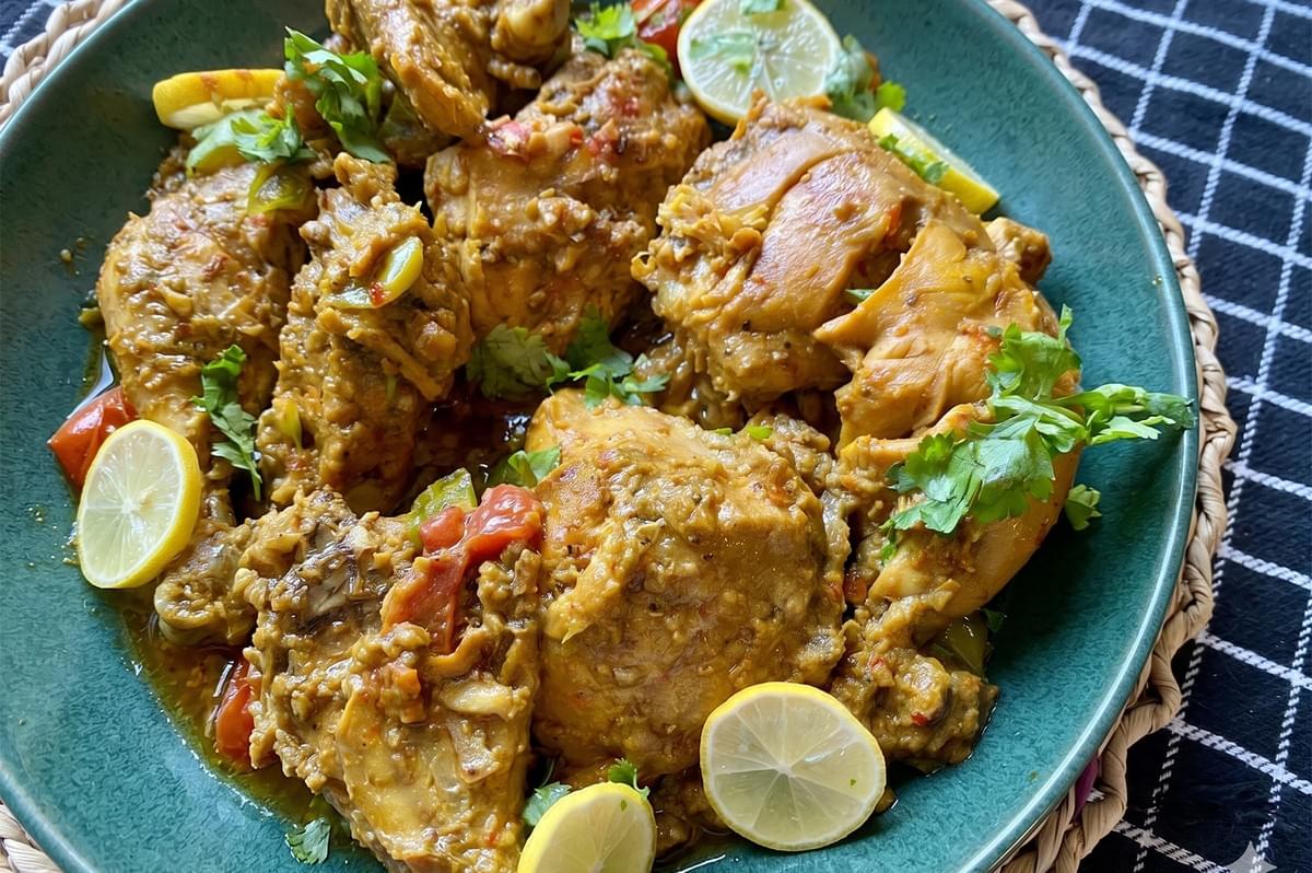 Spiced chicken karahi garnished with fresh cilantro and lemon slices in a teal serving bowl. Spiced chicken karahi garnished with fresh cilantro and lemon slices in a teal serving bowl.