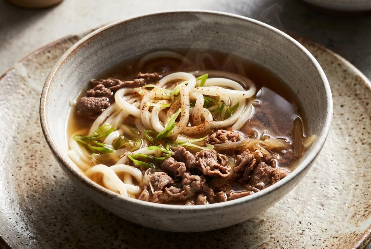 Bowl of hot beef udon noodle soup garnished with sliced green onions and spice powder. Bowl of hot beef udon noodle soup garnished with sliced green onions and spice powder.