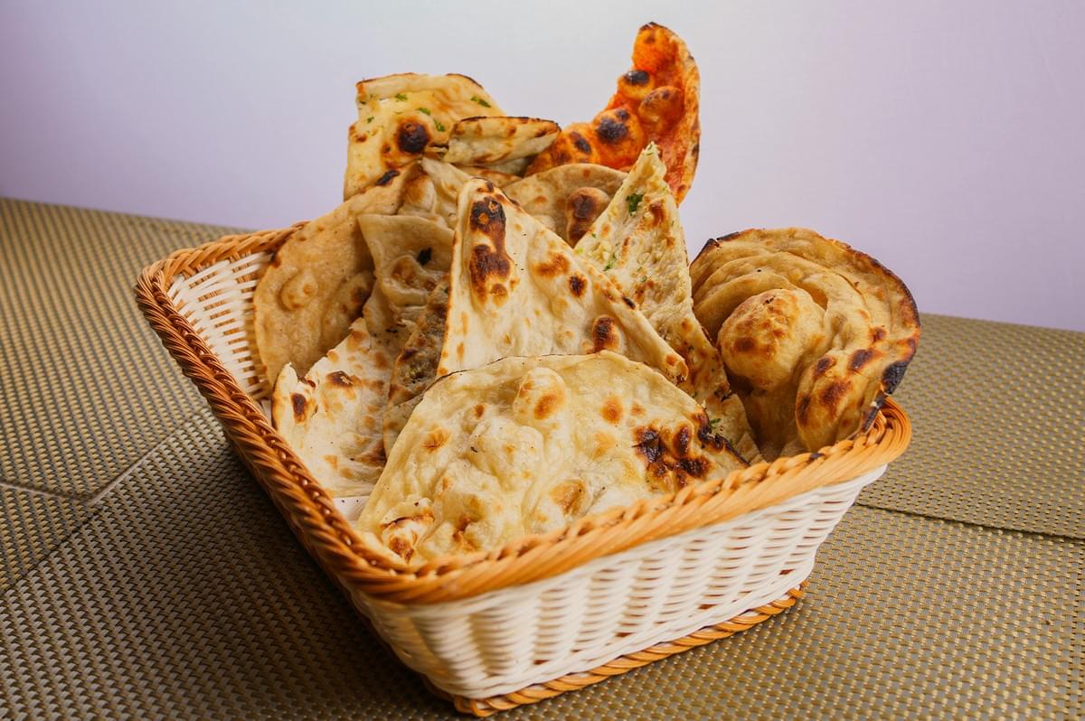 A basket of assorted breads, including butter naan, garlic naan, and tandoori roti, served in a woven wicker basket. A basket of assorted breads, including butter naan, garlic naan, and tandoori roti, served in a woven wicker basket.