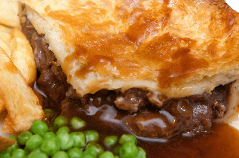 A close-up of a meat pie served with a side of bright green mushy peas and golden fries, topped with rich brown gravy seeping from the pastry. A close-up of a meat pie served with a side of bright green mushy peas and golden fries, topped with rich brown gravy seeping from the pastry.