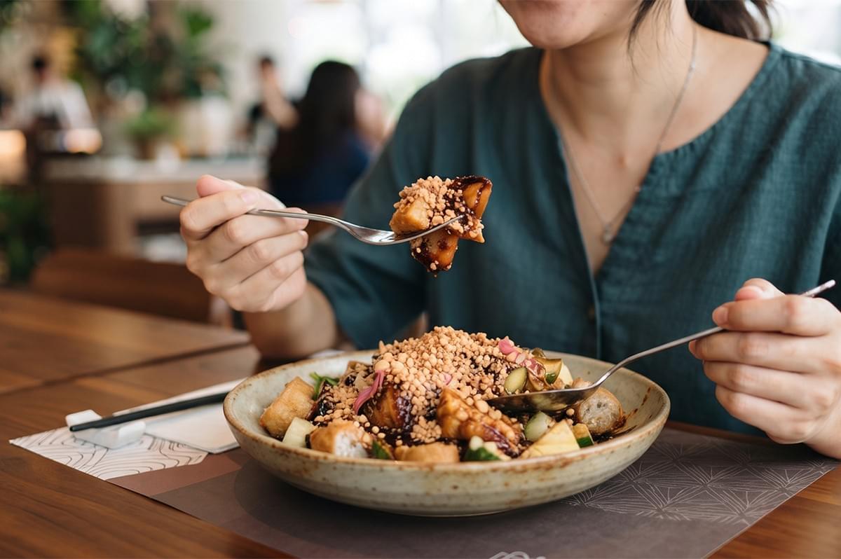 A person eating rojak, a traditional Southeast Asian fruit and vegetable salad topped with crushed peanuts and savory sauce, in a restaurant. A person eating rojak, a traditional Southeast Asian fruit and vegetable salad topped with crushed peanuts and savory sauce, in a restaurant.