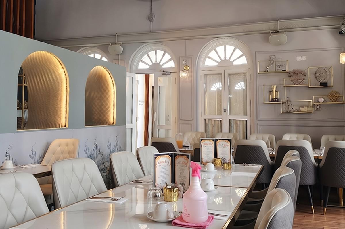 Interior view of The White Label SG French restaurant featuring elegant white and grey dining furniture, arched windows, and chic gold wall shelving. Interior view of The White Label SG French restaurant featuring elegant white and grey dining furniture, arched windows, and chic gold wall shelving.