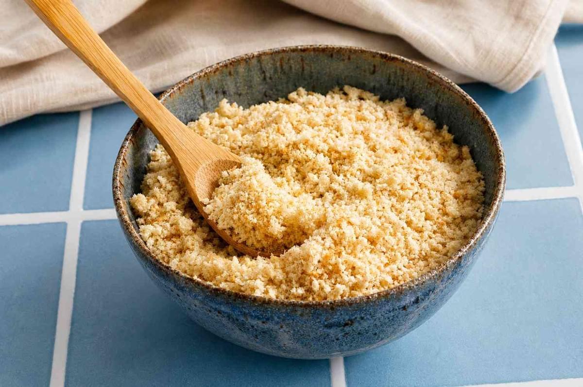 Fresh breadcrumbs in a ceramic bowl with a wooden spoon on a blue tiled table. Fresh breadcrumbs in a ceramic bowl with a wooden spoon on a blue tiled table.