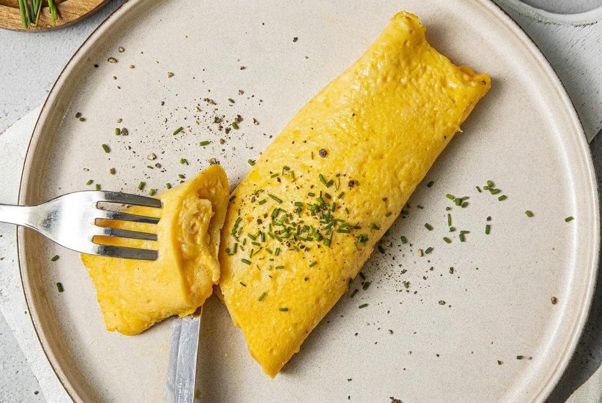 French omelet sprinkled with fresh herbs and black pepper served on a ceramic plate. French omelet sprinkled with fresh herbs and black pepper served on a ceramic plate.