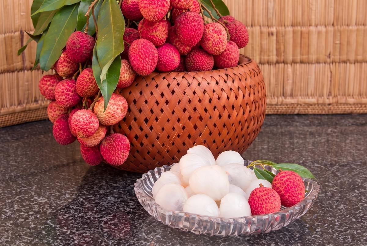 Glass bowl of peeled lychees in front of a woven basket full of fresh lychees. Glass bowl of peeled lychees in front of a woven basket full of fresh lychees.