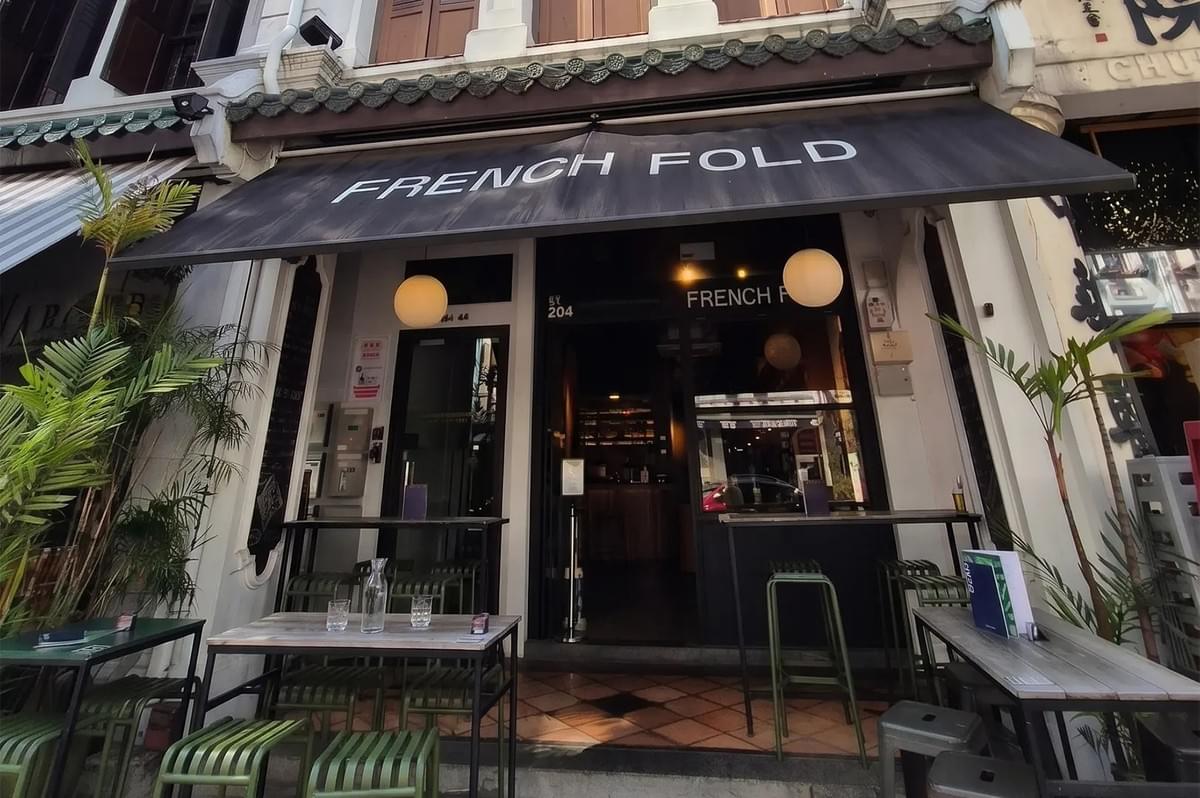 French Fold restaurant storefront with a black awning and outdoor seating tables. French Fold restaurant storefront with a black awning and outdoor seating tables.