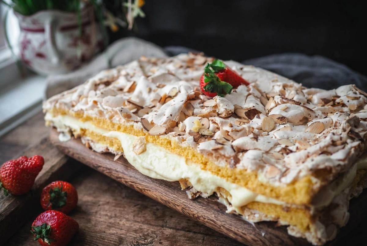 Rectangular layer cake filled with vanilla cream, topped with meringue, sliced almonds, and fresh strawberries. Rectangular layer cake filled with vanilla cream, topped with meringue, sliced almonds, and fresh strawberries.
