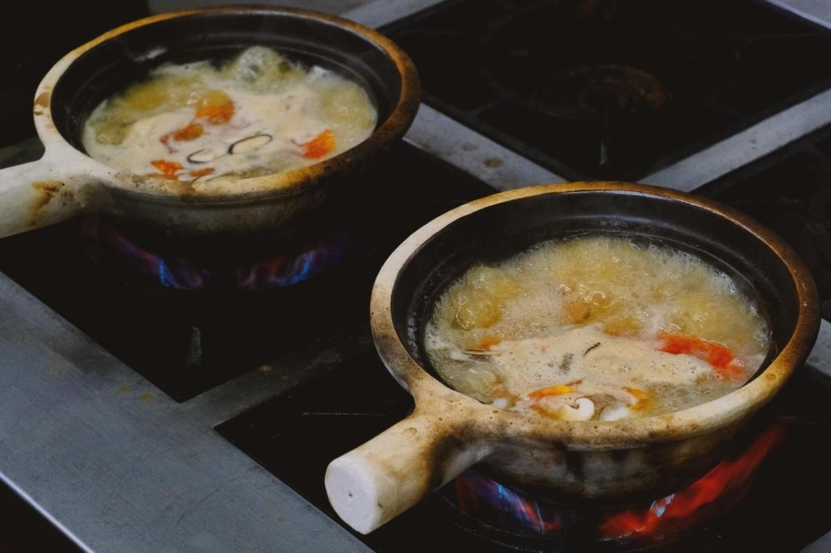 Two claypots containing pomfret fish soup being cooked on stove top Two claypots containing pomfret fish soup being cooked on stove top