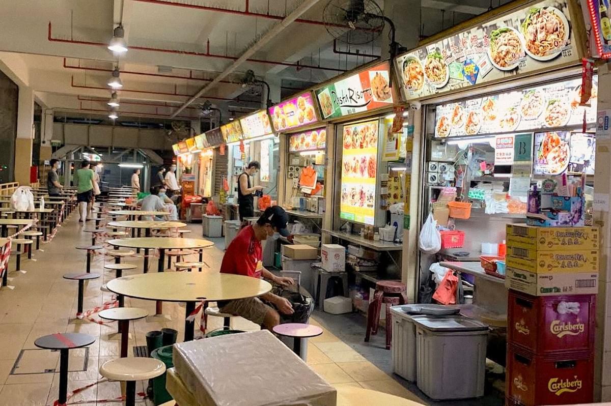 A busy Southeast Asian hawker center lined with food stalls, colorful menu boards, and communal dining tables. A busy Southeast Asian hawker center lined with food stalls, colorful menu boards, and communal dining tables.