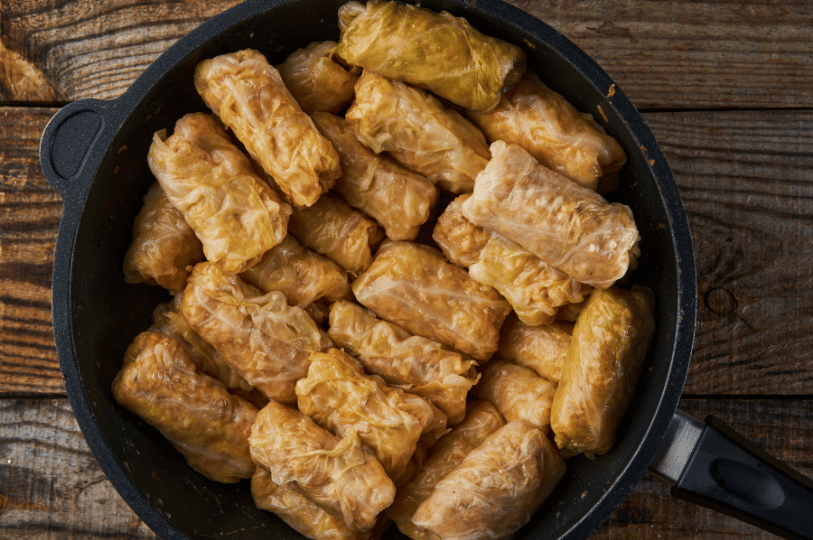 A top-down view of a black pan completely filled with homemade cooked cabbage rolls on a rustic wooden table. A top-down view of a black pan completely filled with homemade cooked cabbage rolls on a rustic wooden table.