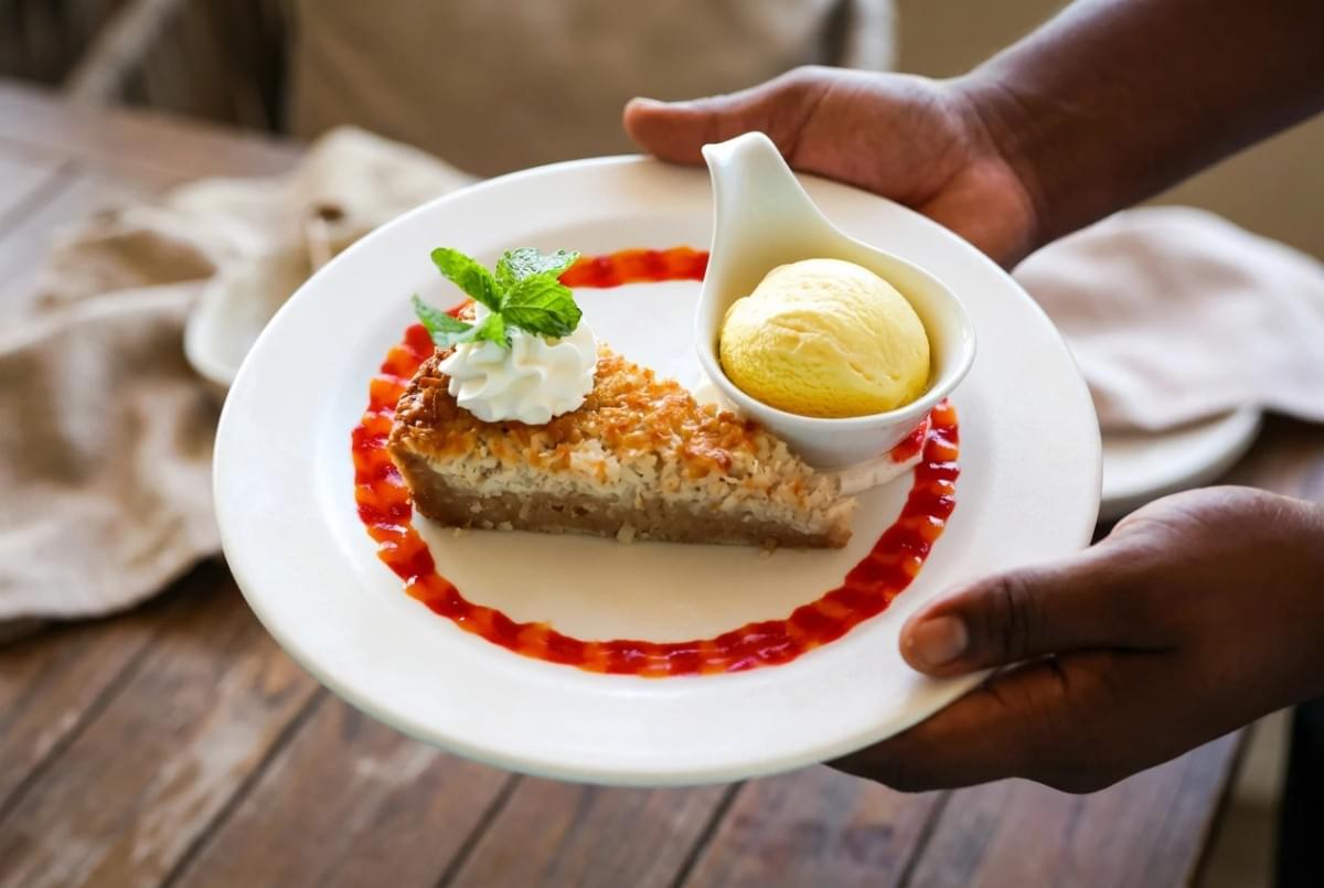 Slice of coconut tart served on a white plate with whipped cream, red fruit drizzle, and vanilla ice cream. Slice of coconut tart served on a white plate with whipped cream, red fruit drizzle, and vanilla ice cream.