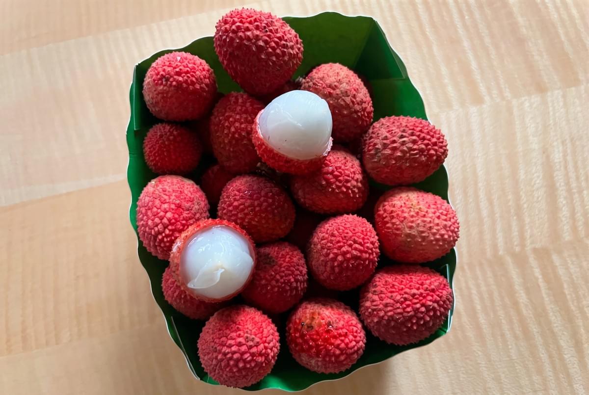Container filled with red lychees, including two partially peeled showing white fruit. Container filled with red lychees, including two partially peeled showing white fruit.