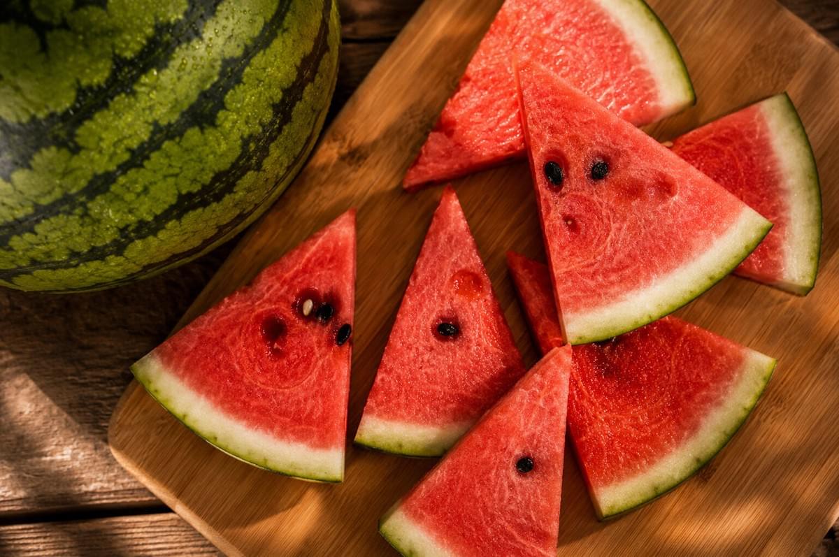 Freshly cut triangular watermelon slices arranged flat on a wooden cutting board next to a whole watermelon. Freshly cut triangular watermelon slices arranged flat on a wooden cutting board next to a whole watermelon.