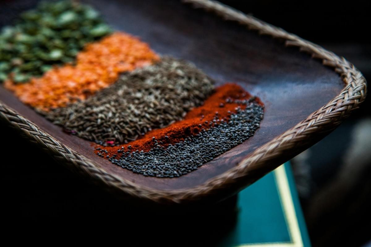 A wooden tray with a woven border holds distinct stripes of colorful seeds, spices, and lentils. The shallow-focus shot highlights dark chia seeds, bright red spice powder, brown cumin seeds, orange red lentils, and green pumpkin seeds in neat rows. A wooden tray with a woven border holds distinct stripes of colorful seeds, spices, and lentils. The shallow-focus shot highlights dark chia seeds, bright red spice powder, brown cumin seeds, orange red lentils, and green pumpkin seeds in neat rows.