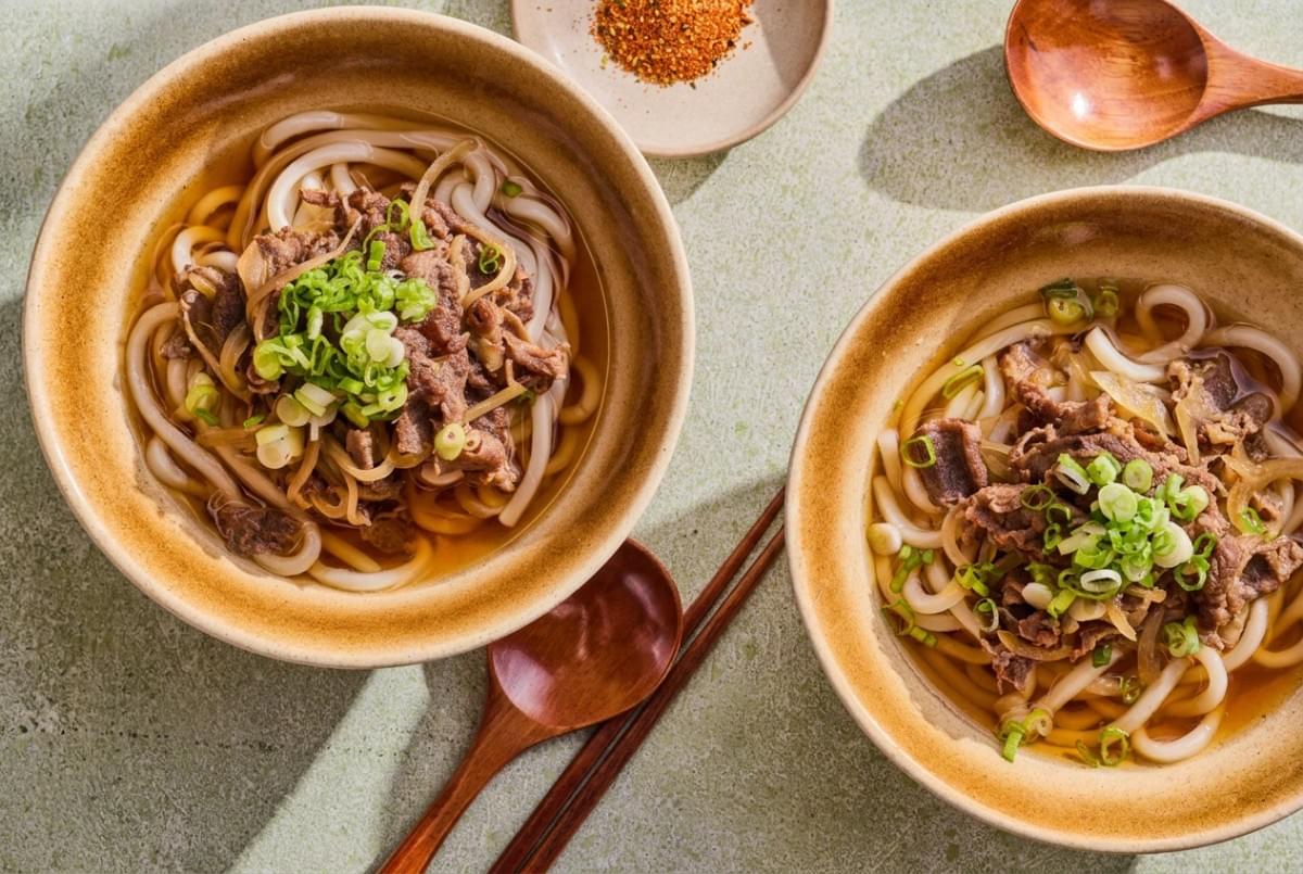 Flat lay of two bowls of beef udon soup with green onions, wooden spoons, and chopsticks. Flat lay of two bowls of beef udon soup with green onions, wooden spoons, and chopsticks.