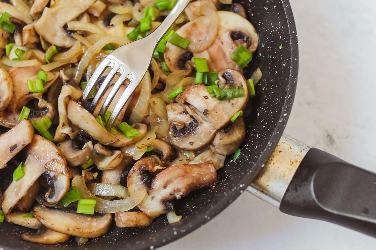 Stir-fried white mushrooms and spring onions in a pan. Stir-fried white mushrooms and spring onions in a pan.