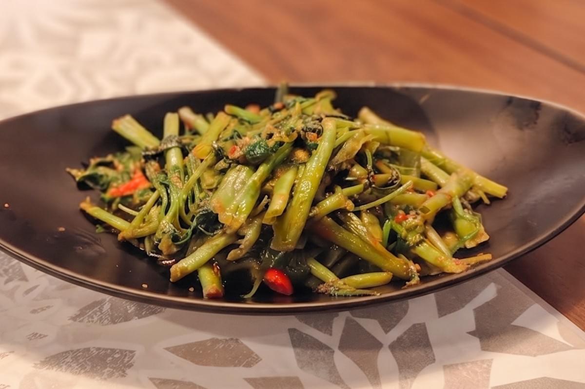 Spicy stir-fried sambal kangkong greens served on a black plate. Spicy stir-fried sambal kangkong greens served on a black plate.