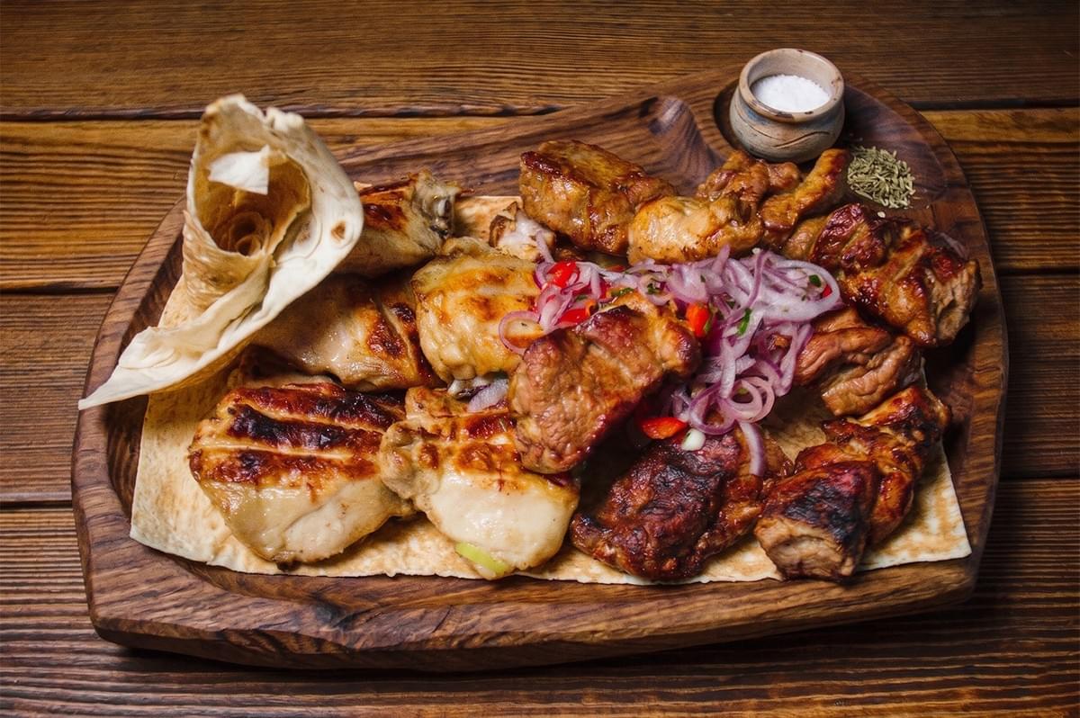 An assortment of grilled meats including chicken and pork skewers served on flatbread with red onions and spices on a wooden platter. An assortment of grilled meats including chicken and pork skewers served on flatbread with red onions and spices on a wooden platter.