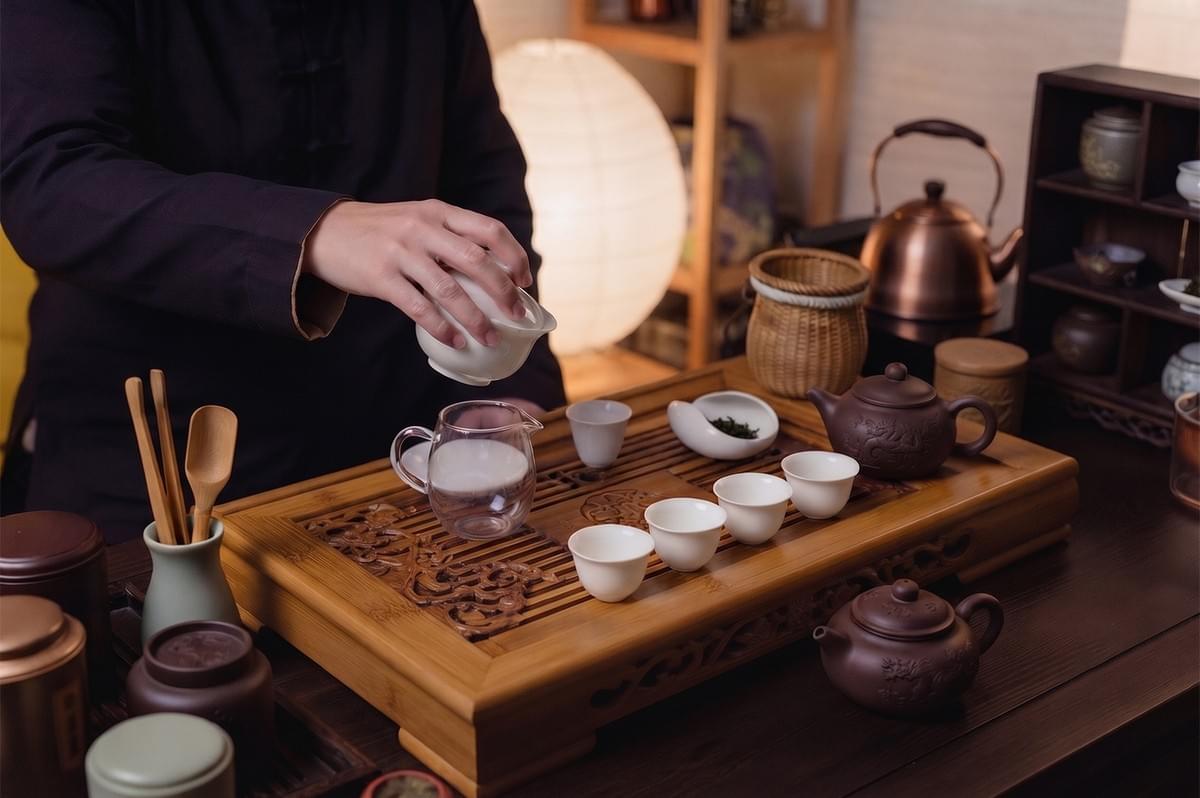 A person performing a traditional Chinese tea ceremony by pouring tea into a glass server on a carved wooden tray. A person performing a traditional Chinese tea ceremony by pouring tea into a glass server on a carved wooden tray.