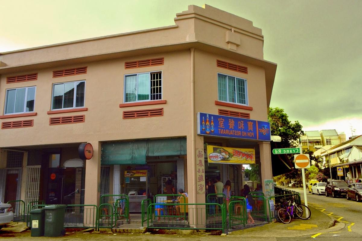 Street corner with a beige two-story building housing a restaurant. A blue sign with a neon light is above the entrance. Bicycles are parked nearby. Street corner with a beige two-story building housing a restaurant. A blue sign with a neon light is above the entrance. Bicycles are parked nearby.
