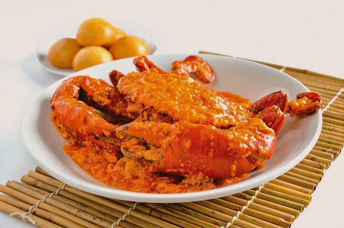 A whole crab covered in glossy orange-red sauce served on a white plate with citrus fruit in the background. A whole crab covered in glossy orange-red sauce served on a white plate with citrus fruit in the background.