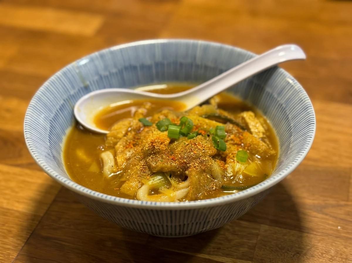 A bowl of Japanese curry udon topped with green onions and chili powder, served with a soup spoon. A bowl of Japanese curry udon topped with green onions and chili powder, served with a soup spoon.