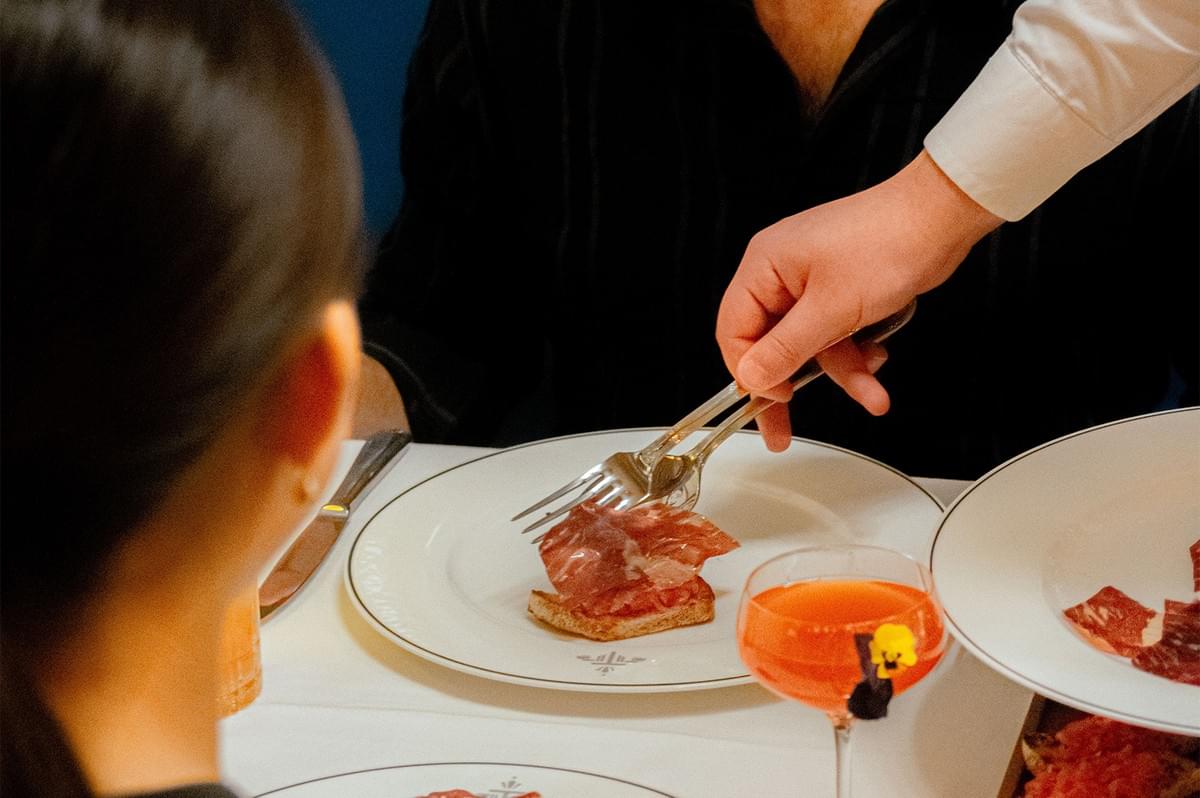Waiter serving a slice of prosciutto on toasted bread at an upscale restaurant. Waiter serving a slice of prosciutto on toasted bread at an upscale restaurant.