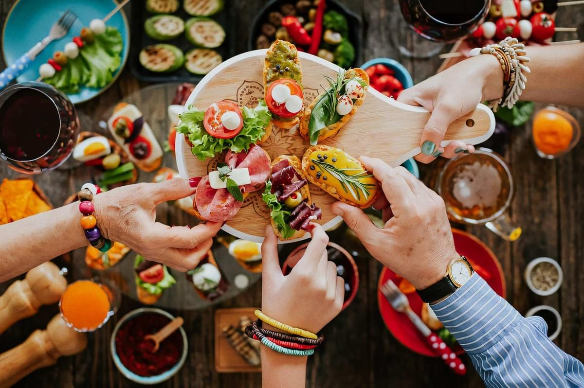 Hands sharing a wooden board of assorted canapés and appetizers with wine. Hands sharing a wooden board of assorted canapés and appetizers with wine.