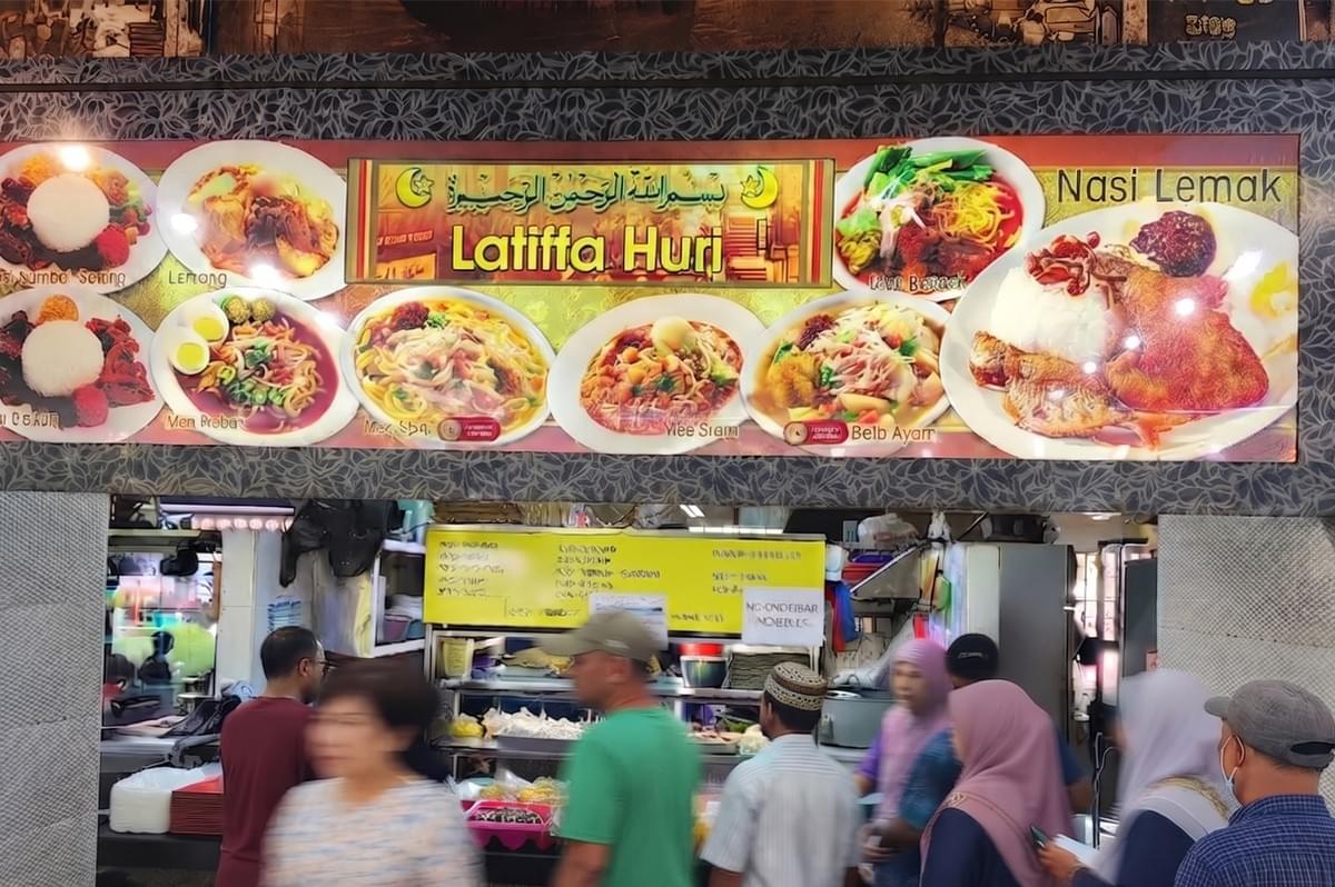 Latiffa Huri food stall storefront with a colorful menu banner displaying Nasi Lemak and noodles, and customers waiting in line. Latiffa Huri food stall storefront with a colorful menu banner displaying Nasi Lemak and noodles, and customers waiting in line.