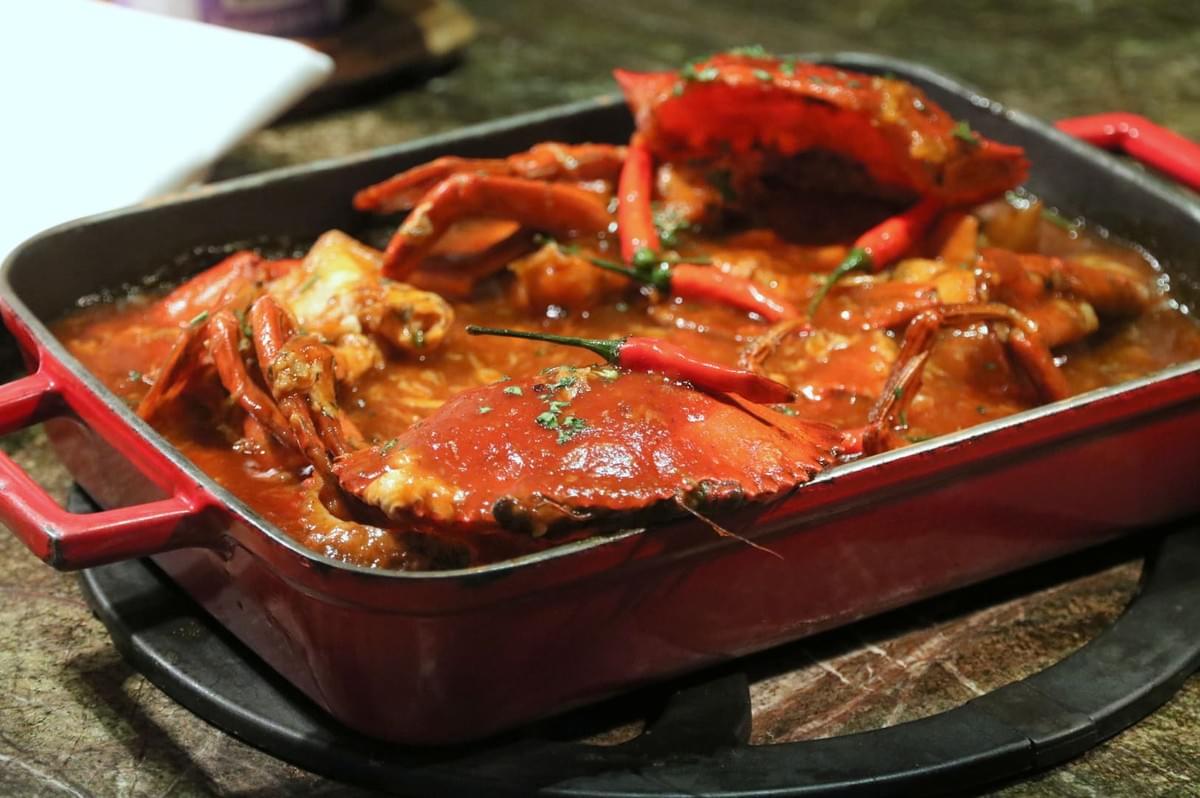A red bowl filled with chili crab, placed on a table, highlighting the dish's rich colors and textures. A red bowl filled with chili crab, placed on a table, highlighting the dish's rich colors and textures.