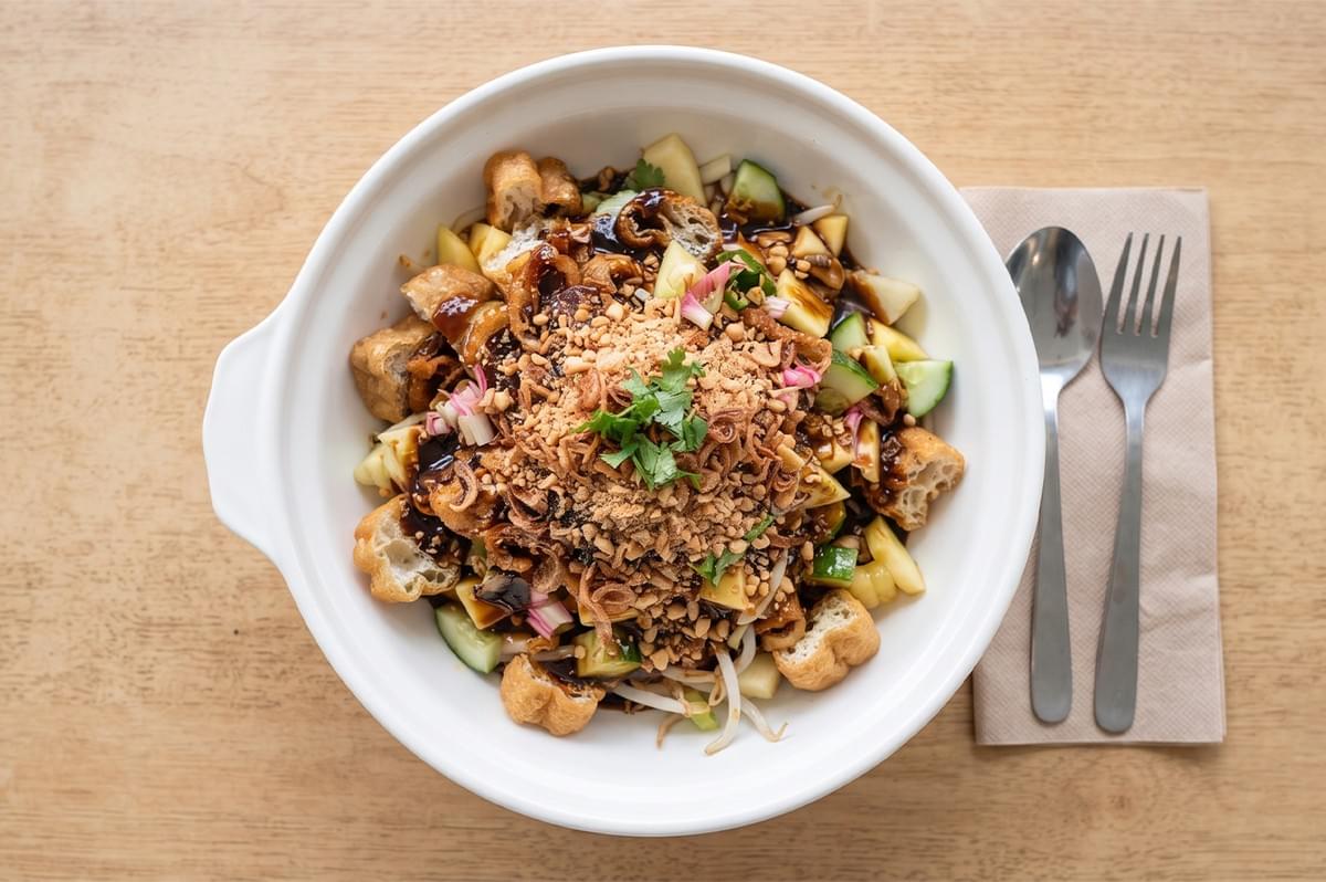 Top-down view of a bowl of rojak salad with fried dough fritters, cucumber, fruits, crushed peanuts, and dark sauce. Top-down view of a bowl of rojak salad with fried dough fritters, cucumber, fruits, crushed peanuts, and dark sauce.