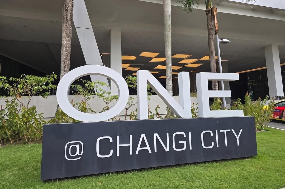 Exterior view of the ONE @ Changi City building signage in Singapore with modern architecture and palm trees. Exterior view of the ONE @ Changi City building signage in Singapore with modern architecture and palm trees.