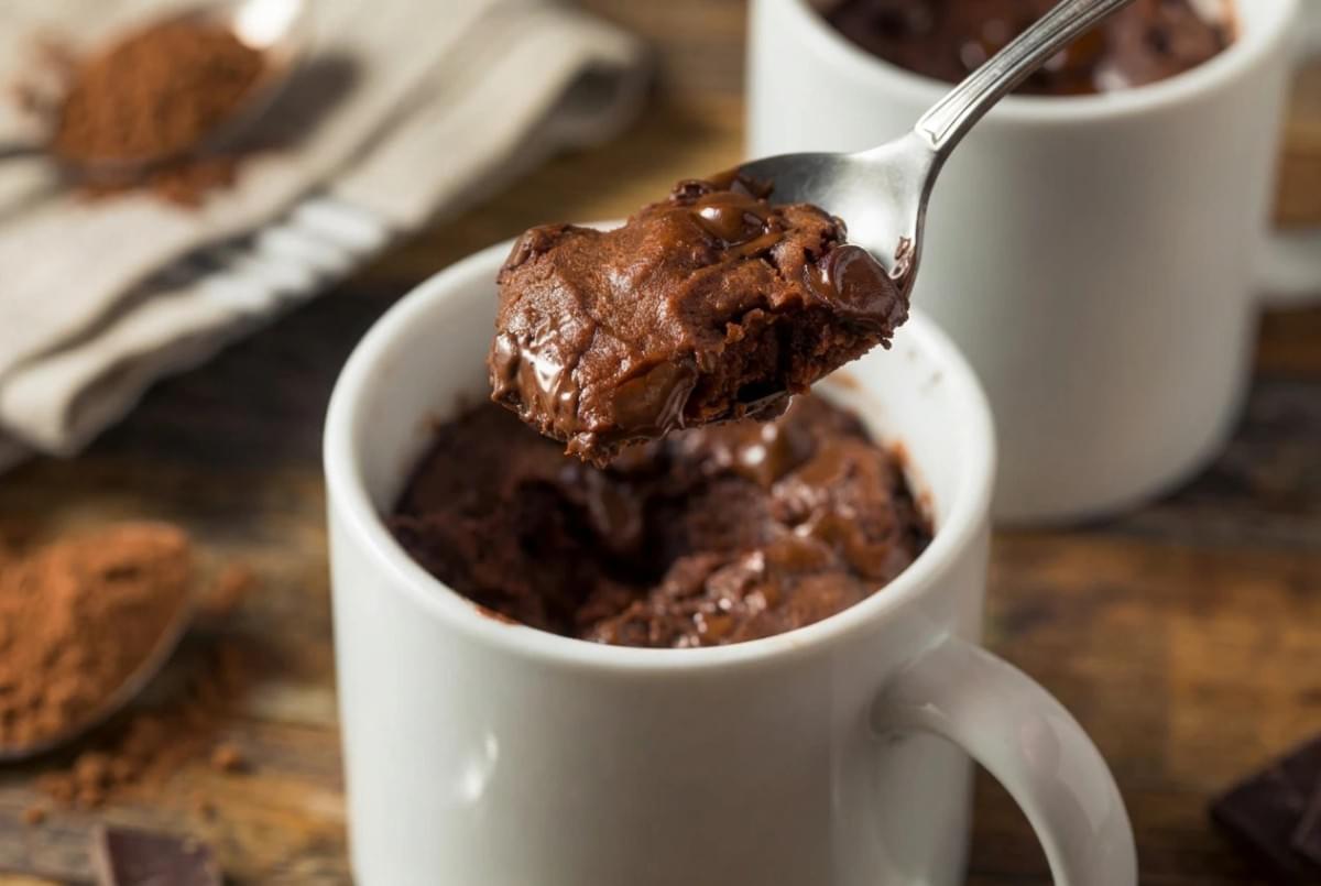 Spoon scooping a warm, gooey chocolate chip mug cake out of a white ceramic cup. Spoon scooping a warm, gooey chocolate chip mug cake out of a white ceramic cup.