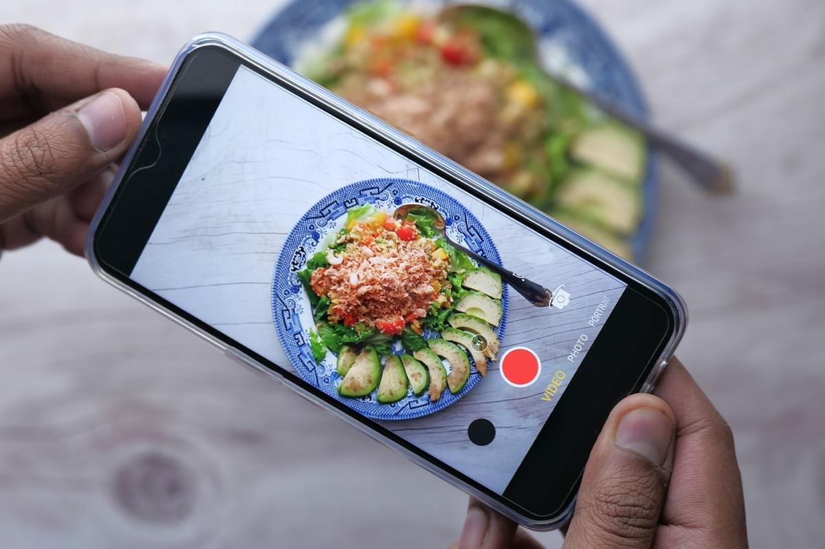 Person holding a smartphone recording a video of a fresh food dish for a social media halal food review. Person holding a smartphone recording a video of a fresh food dish for a social media halal food review.