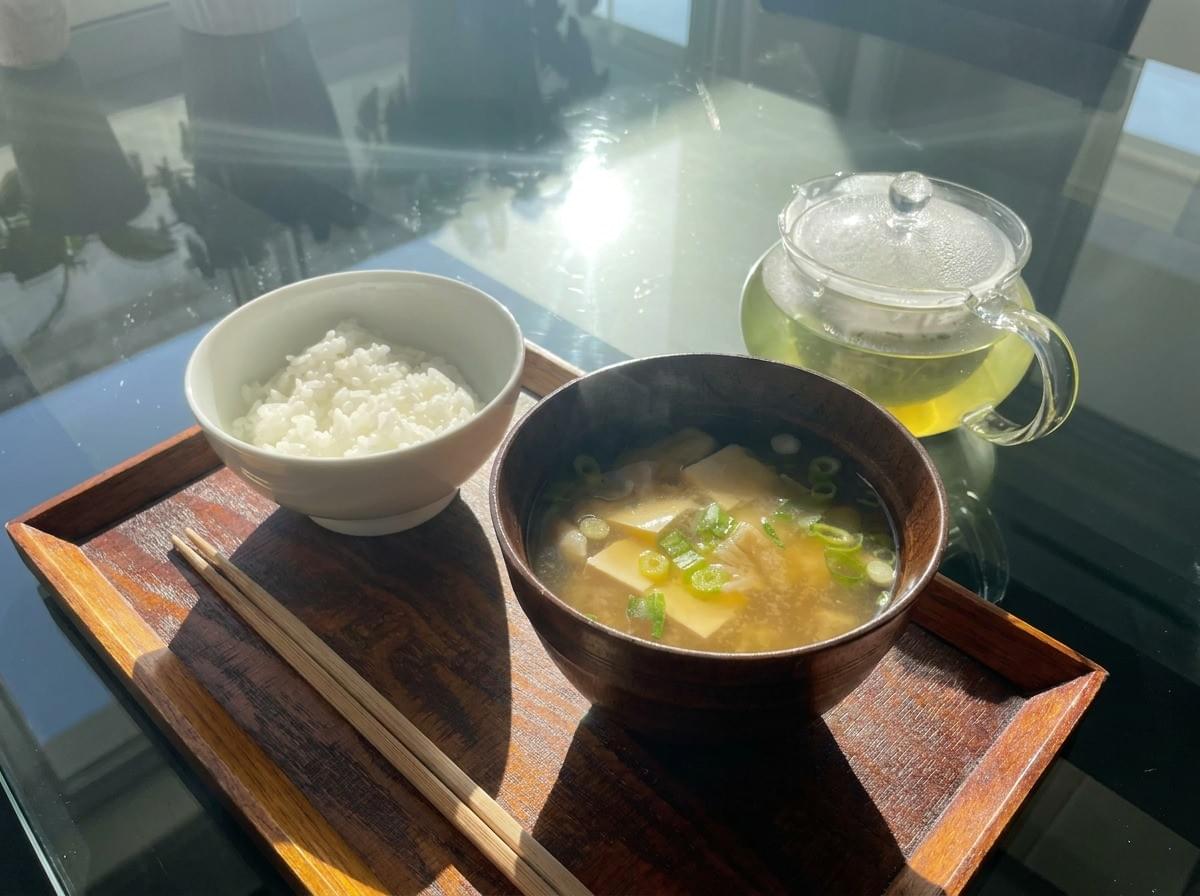 A wooden tray set with a bowl of miso soup, a bowl of white rice, chopsticks, and a teapot. A wooden tray set with a bowl of miso soup, a bowl of white rice, chopsticks, and a teapot.