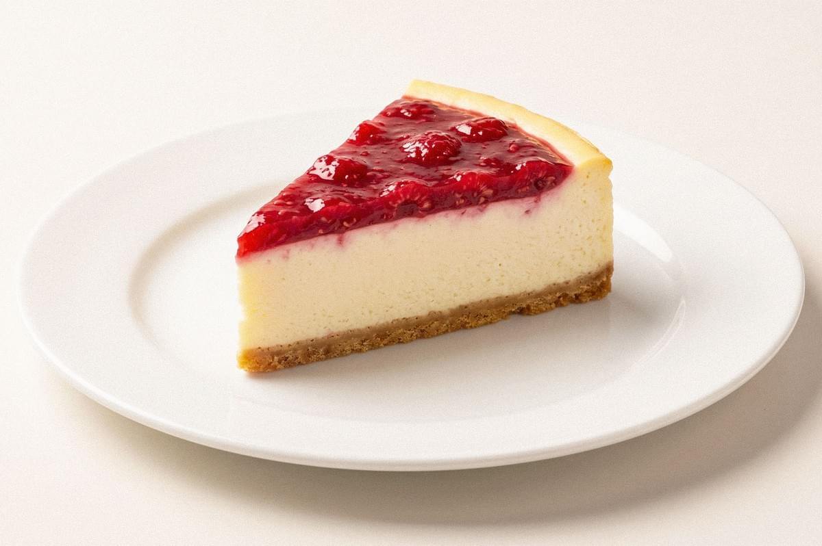 A slice of cheesecake topped with glossy red berry sauce on a white plate A slice of cheesecake topped with glossy red berry sauce on a white plate