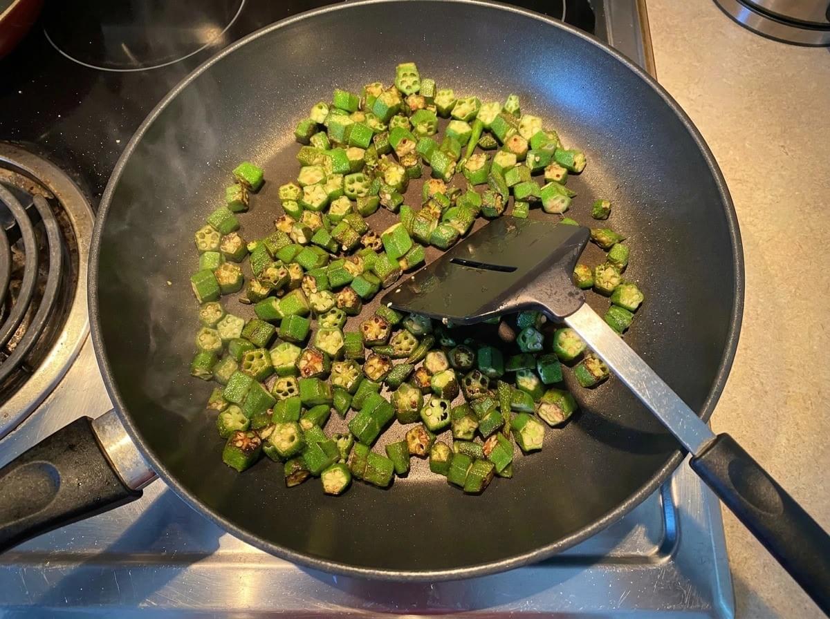 A top-down close-up shot of crispy, golden-brown fried okra slices served in a rustic brown ceramic bowl, placed next to a matching saucer with small whole red chili peppers. A top-down close-up shot of crispy, golden-brown fried okra slices served in a rustic brown ceramic bowl, placed next to a matching saucer with small whole red chili peppers.