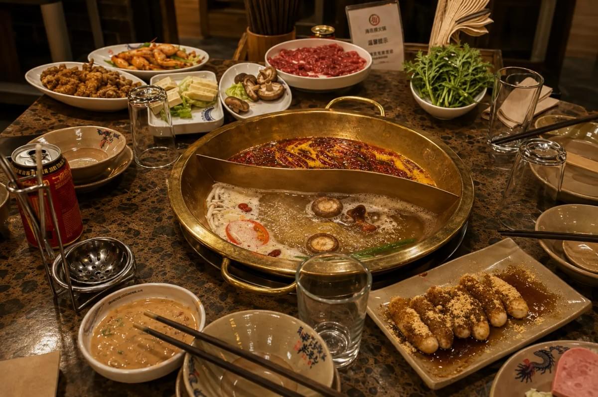 Large feast featuring a central split hot pot surrounded by colorful bowls of raw meats, corn, vegetables, and tofu. Large feast featuring a central split hot pot surrounded by colorful bowls of raw meats, corn, vegetables, and tofu.