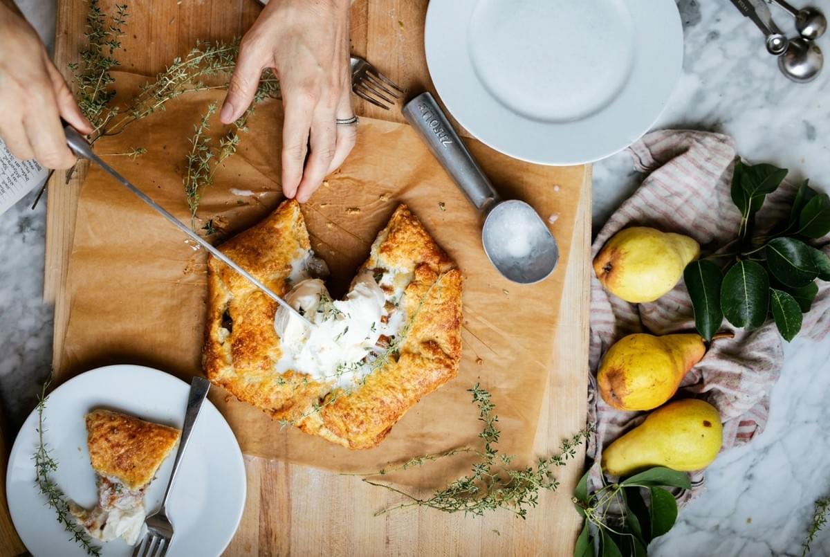 Top-down view of a warm pear galette topped with vanilla ice cream, served alongside fresh pears and sprigs of thyme. Top-down view of a warm pear galette topped with vanilla ice cream, served alongside fresh pears and sprigs of thyme.
