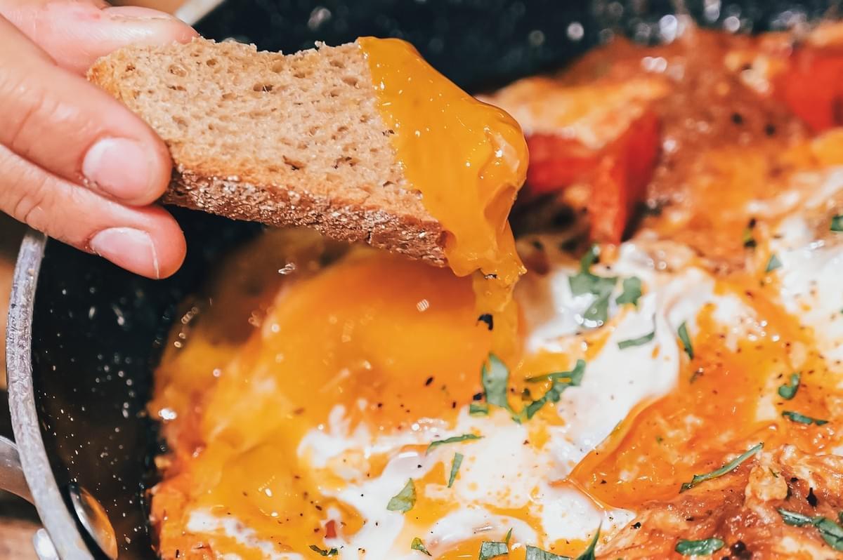 Extreme close-up macro shot of Israeli shakshuka with runny egg yolk, crusty bread dipping into spiced tomato sauce, garnished with fresh herbs in a rustic skillet Extreme close-up macro shot of Israeli shakshuka with runny egg yolk, crusty bread dipping into spiced tomato sauce, garnished with fresh herbs in a rustic skillet
