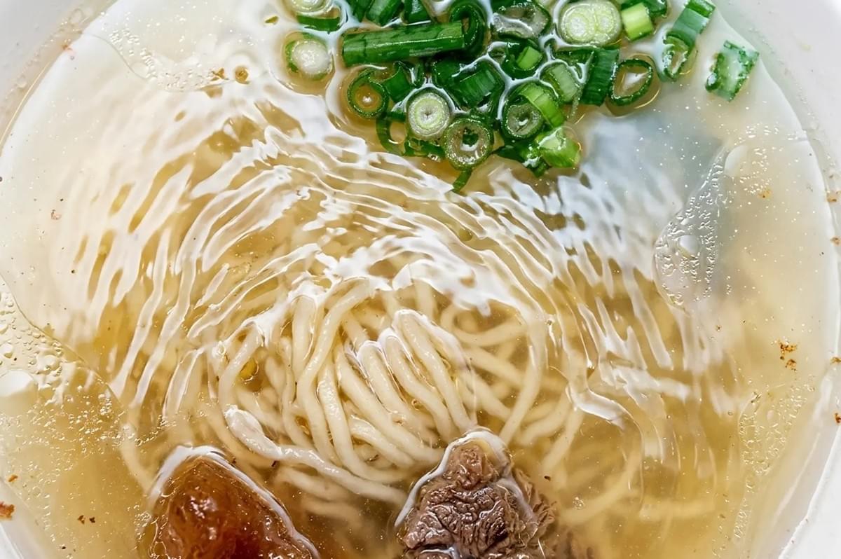 Close-up top view of clear broth noodle soup with green onions and braised beef Close-up top view of clear broth noodle soup with green onions and braised beef