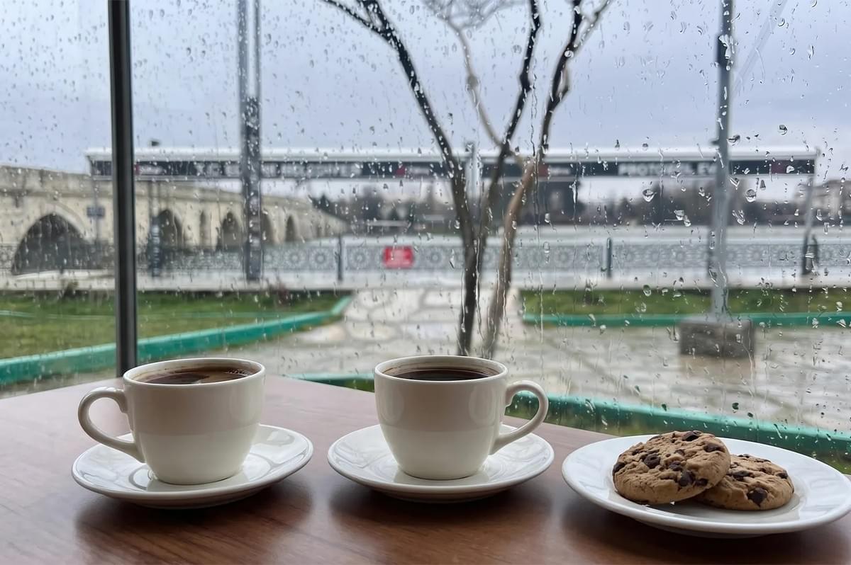 Two cups of coffee and chocolate chip cookies on a table by a rainy window overlooking a historic stone bridge. Two cups of coffee and chocolate chip cookies on a table by a rainy window overlooking a historic stone bridge.