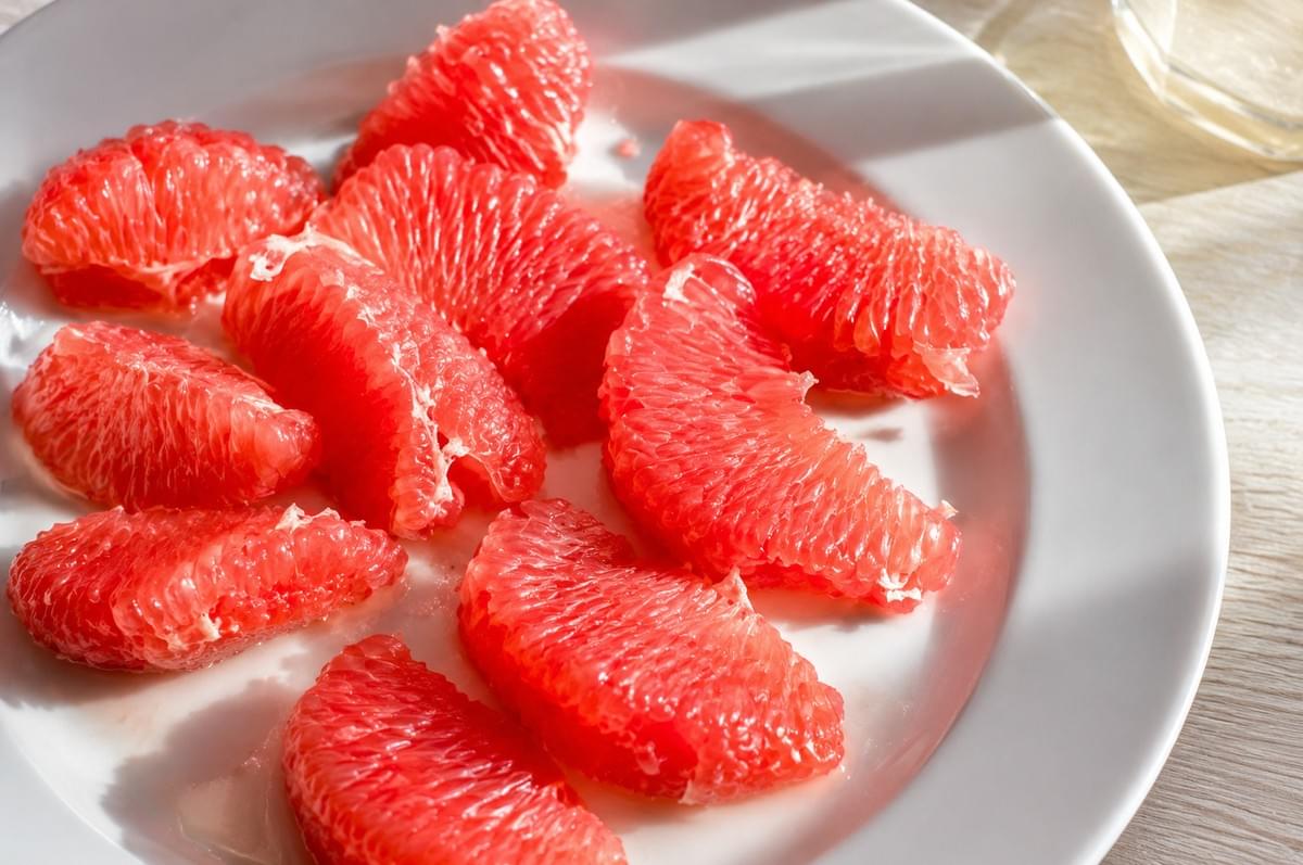 Fresh, peeled pink pomelo segments served on a white plate. Fresh, peeled pink pomelo segments served on a white plate.
