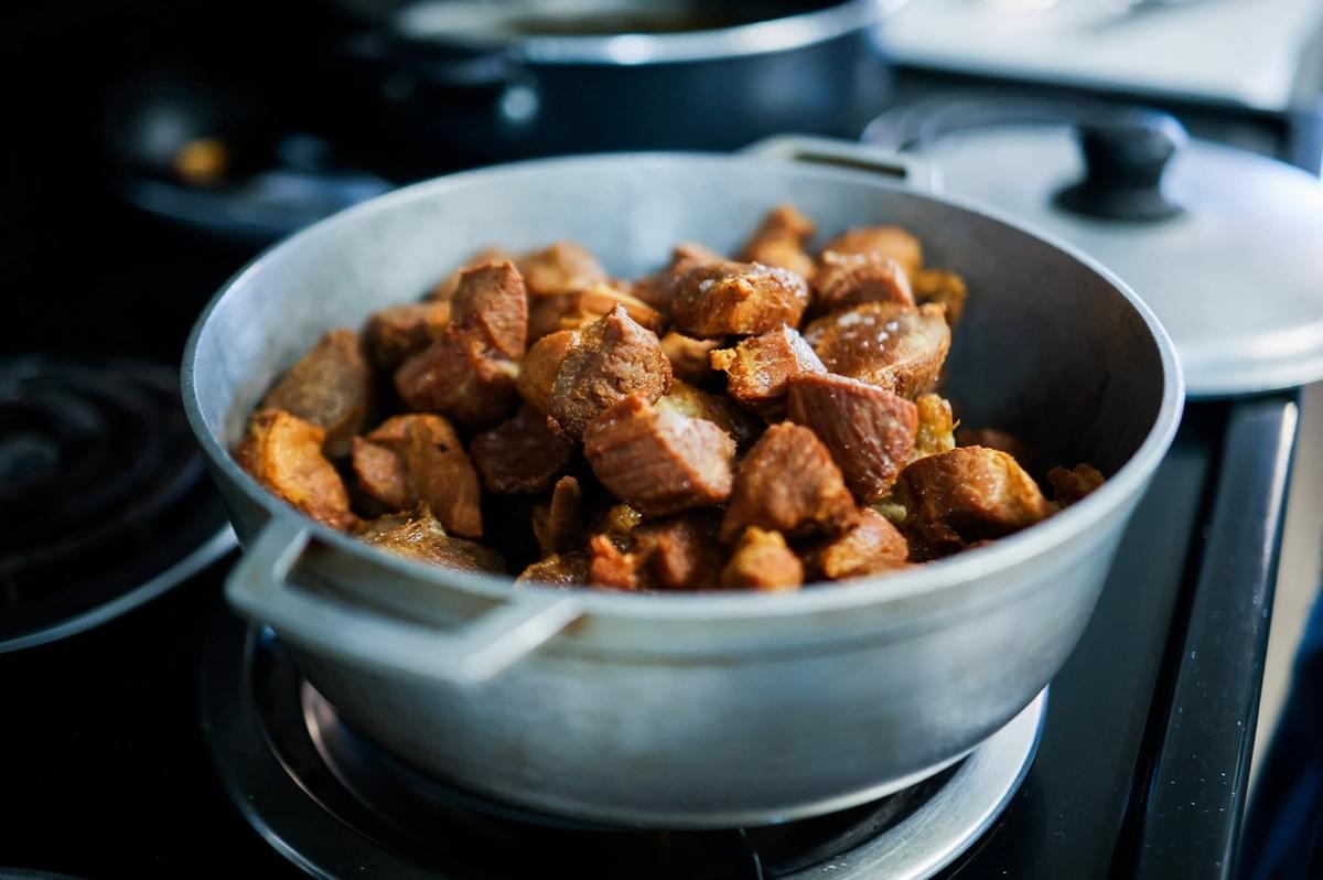 Close-up of a cast-iron pot filled with browned pork belly pieces, ready for braising. Close-up of a cast-iron pot filled with browned pork belly pieces, ready for braising.