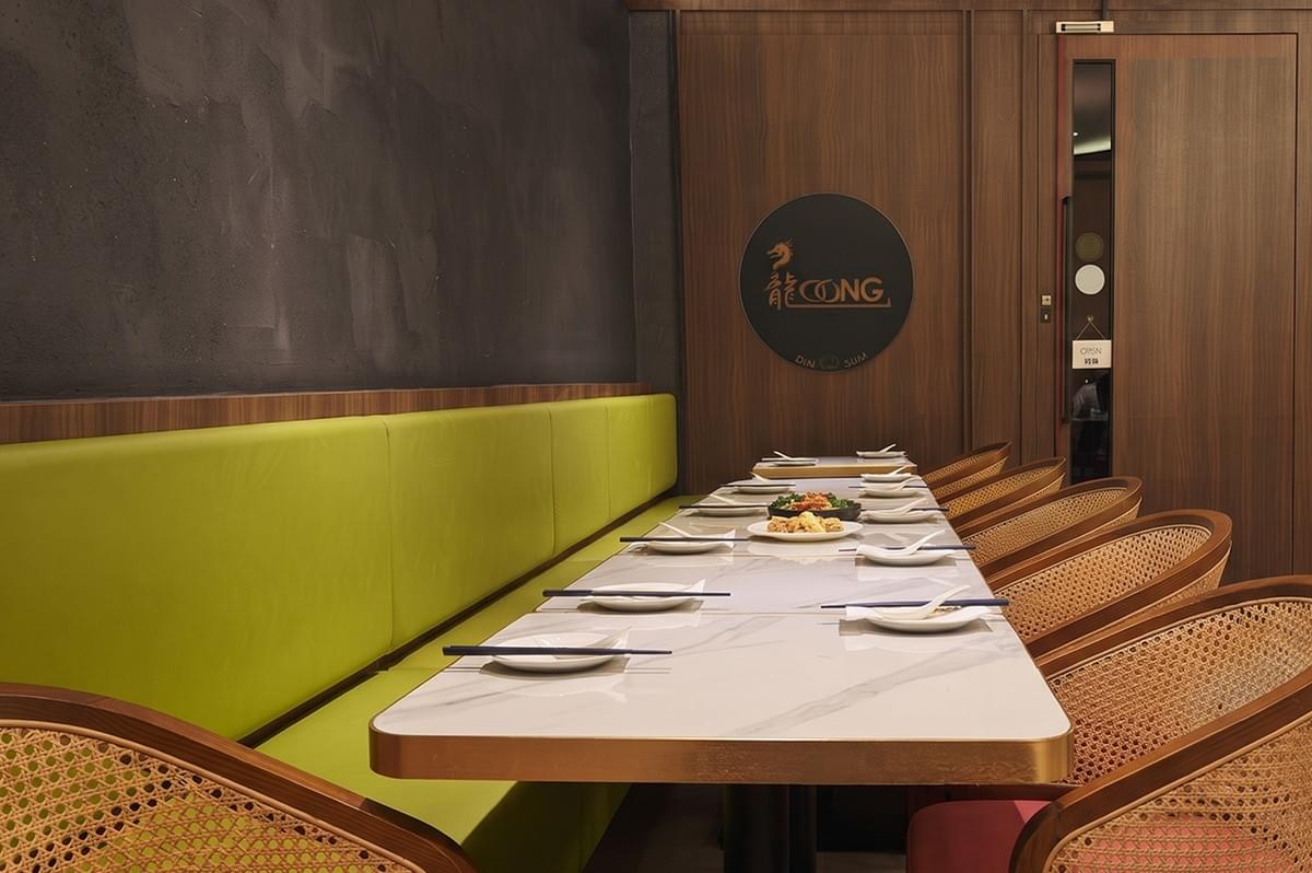 Loong Dim Sum restaurant interior with a long dining table, green booth seating, and wooden chairs. Loong Dim Sum restaurant interior with a long dining table, green booth seating, and wooden chairs.