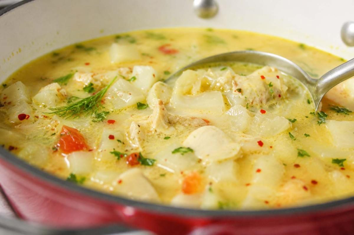 Ladle scooping creamy Icelandic plokkfiskur fish stew with potatoes and herbs from a red pot Ladle scooping creamy Icelandic plokkfiskur fish stew with potatoes and herbs from a red pot