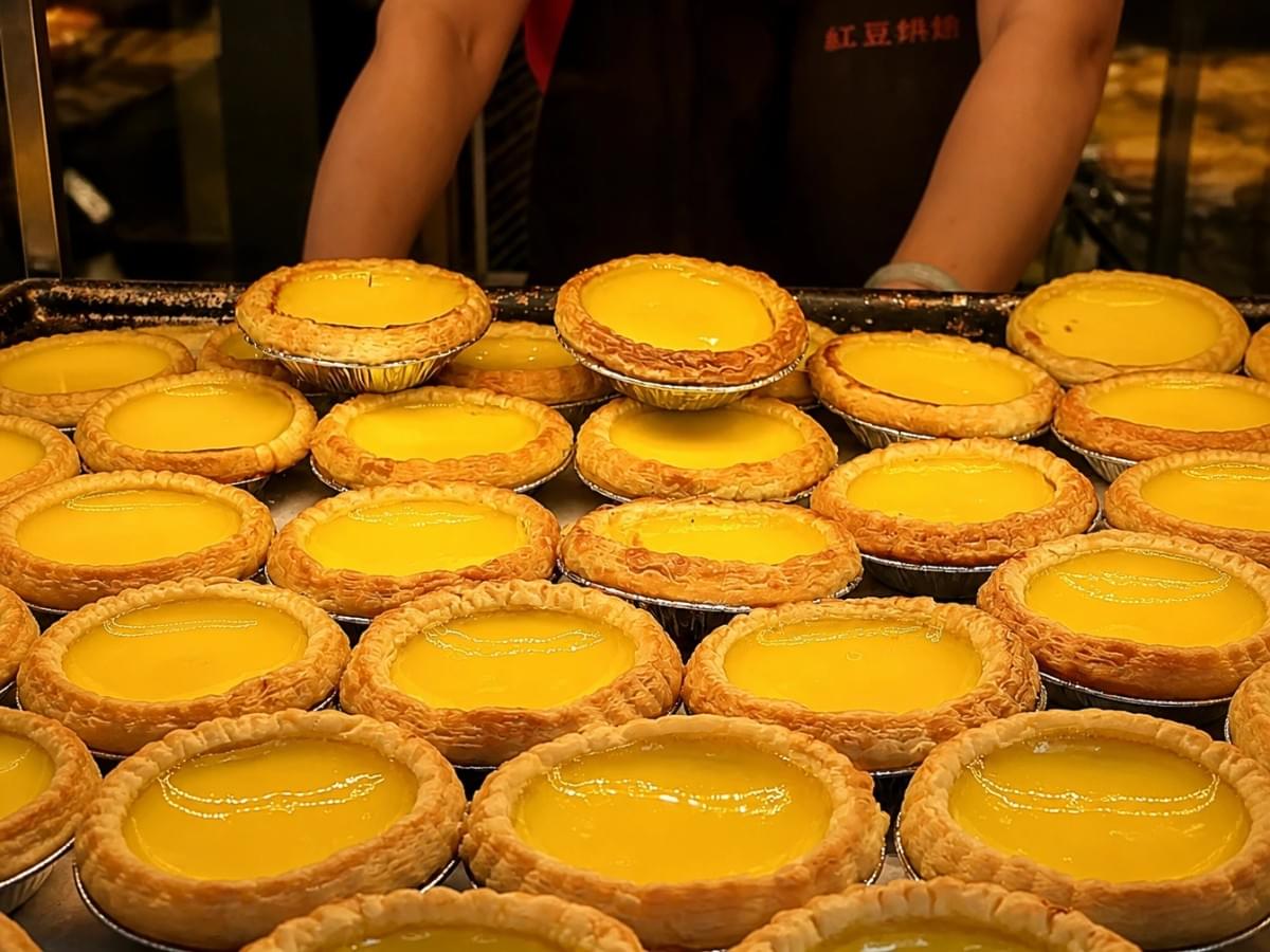 Rows of fresh egg tarts with flaky crusts displayed on a bakery tray. Rows of fresh egg tarts with flaky crusts displayed on a bakery tray.