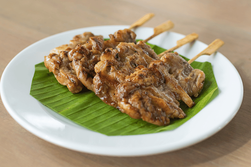A plate of Moo Ping (Thai grilled pork skewers) served on a vibrant green banana leaf, showing charred, caramelized edges from the grill. A plate of Moo Ping (Thai grilled pork skewers) served on a vibrant green banana leaf, showing charred, caramelized edges from the grill.