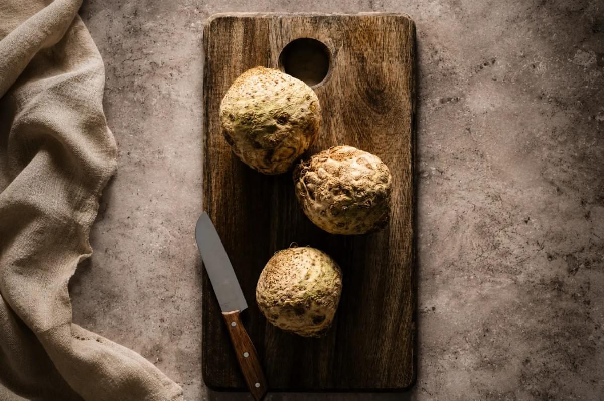 Three celeriac bulbs on a wooden cutting board with a chef's knife. Three celeriac bulbs on a wooden cutting board with a chef's knife.